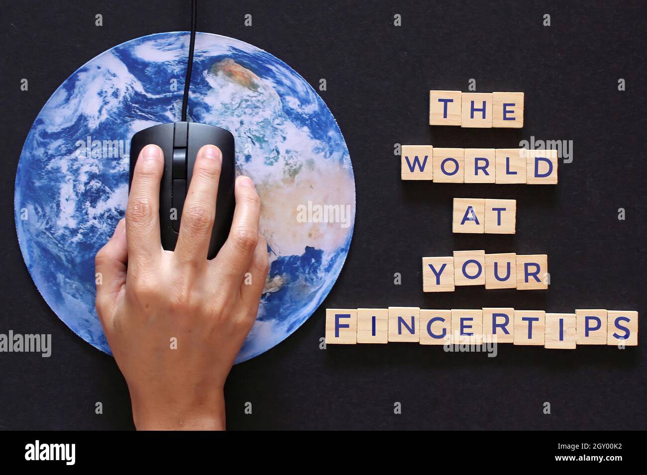 Cliquez à la main la souris d'ordinateur sur la planète Terre globe et cube en bois avec le texte LE MONDE À VOTRE BOUT DES DOIGTS. Banque D'Images