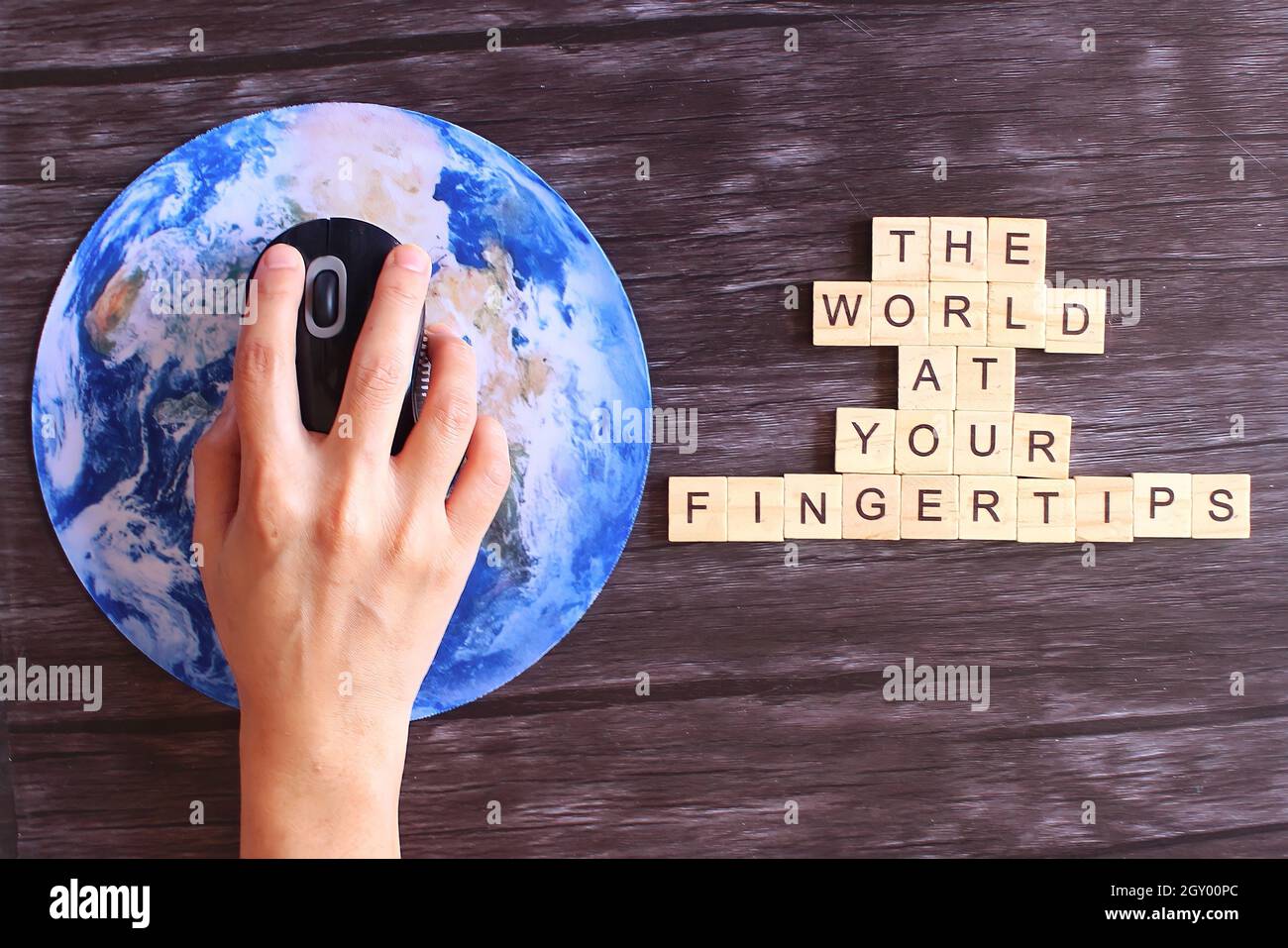Cliquez à la main la souris d'ordinateur sur la planète Terre globe et cube en bois avec le texte LE MONDE À VOTRE BOUT DES DOIGTS. Banque D'Images