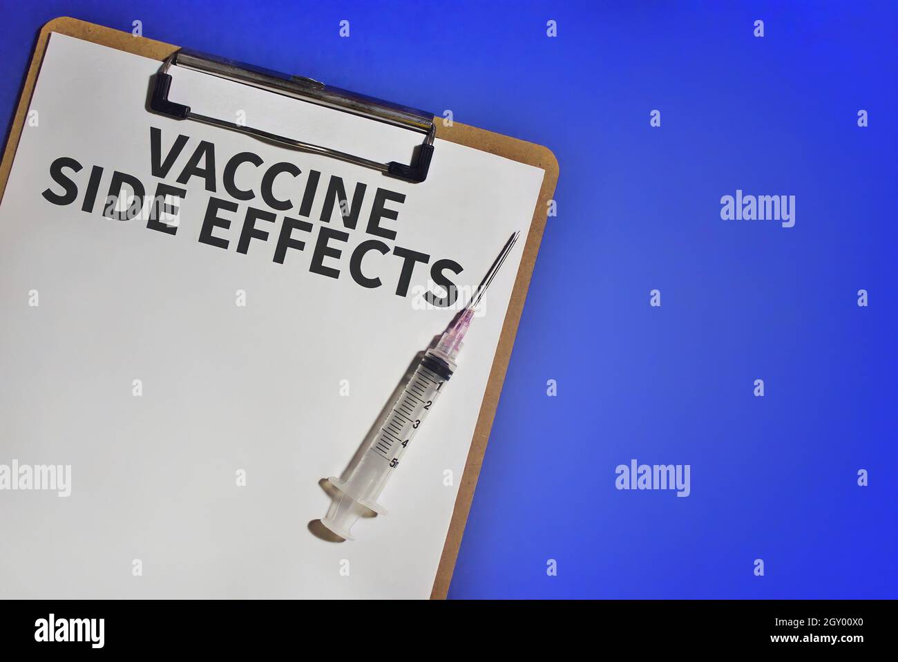 Vue du dessus de la seringue médicale et du presse-papiers avec texte EFFETS SECONDAIRES DU VACCIN sur fond bleu. Copier l'espace pour le texte Banque D'Images