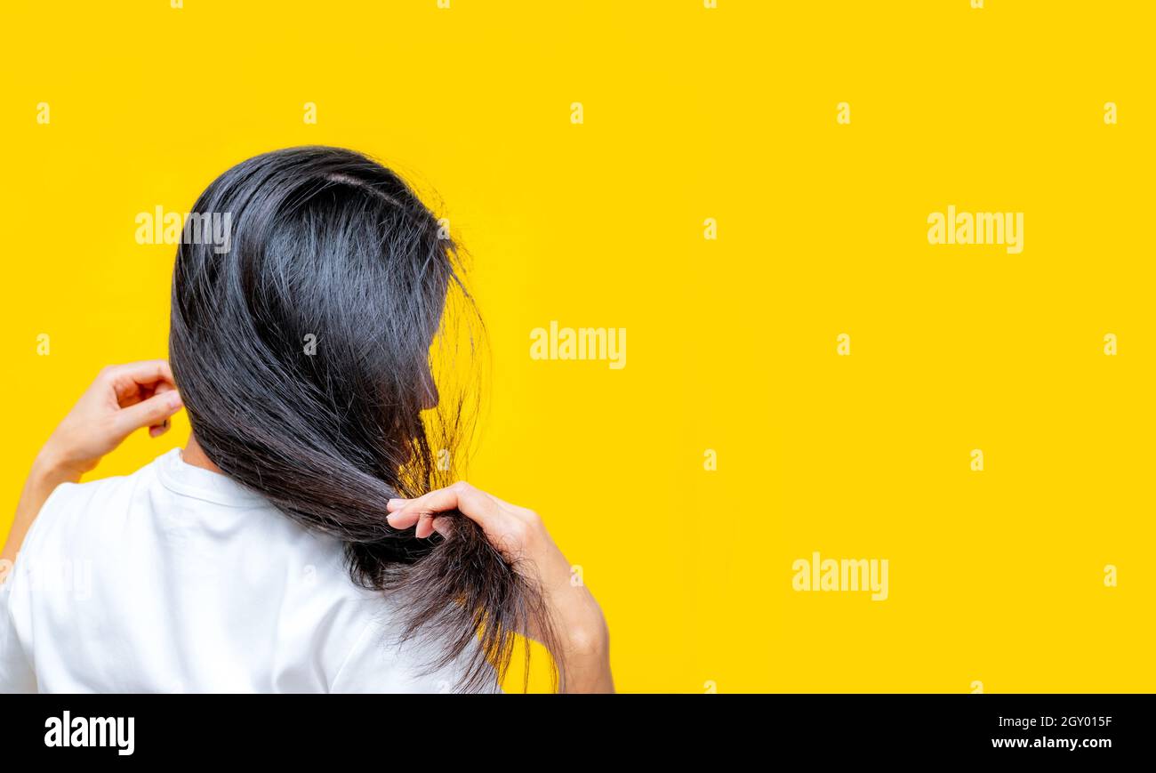 Vue arrière de la femme asiatique tenant les cheveux endommagés sur fond jaune. Perte de cheveux et problème de cheveux minces chez la femme. Les cheveux longs noirs secs et fragiles ont besoin de sha Banque D'Images Vue arrière de la femme asiatique tenant les cheveux endommagés sur fond jaune. Perte de cheveux et problème de cheveux minces chez la femme. Les cheveux longs noirs secs et fragiles ont besoin de sha Banque D'Images
