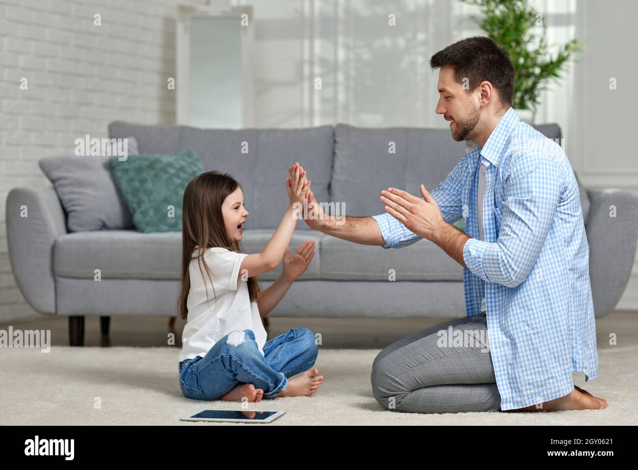 Petite fille joue avec papa à la maison assis sur un tapis blanc. Fête des pères Banque D'Images