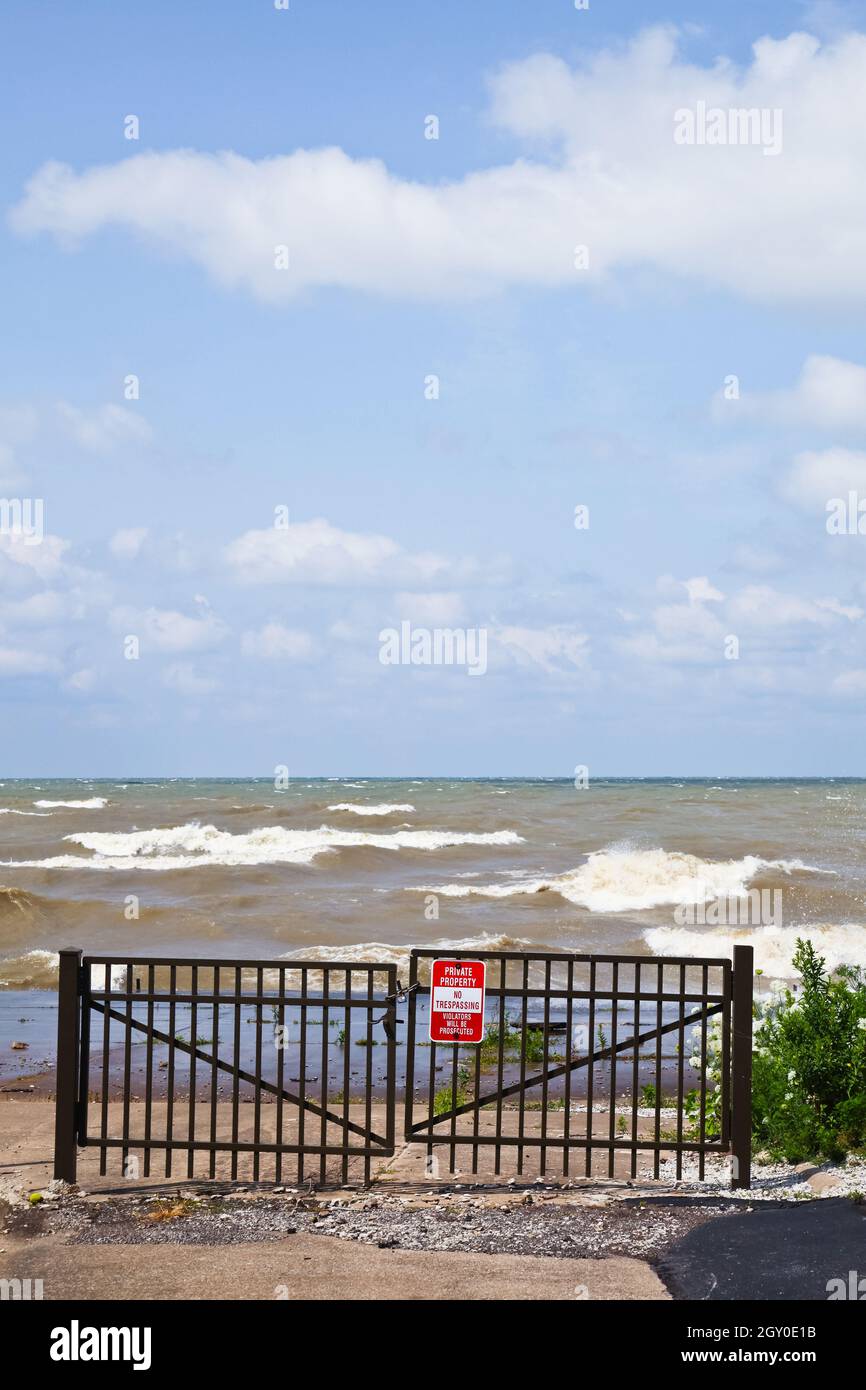 La porte en fer forgé noir est fermée mais montre des vagues moussant blanches et un ciel bleu nuageux Banque D'Images