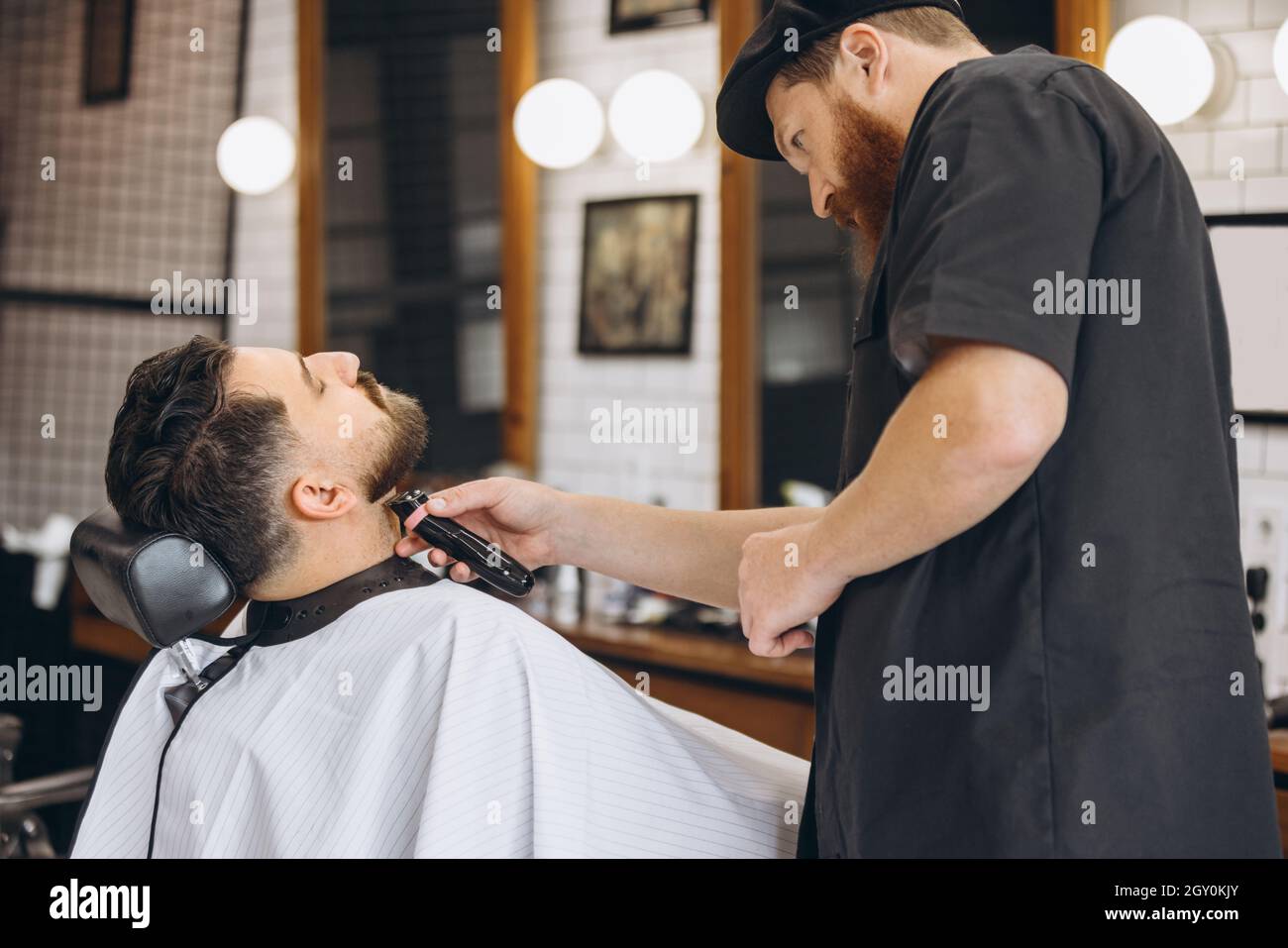 coiffeur professionnel, tondeuse, rasage de la barbe d'un client régulier dans un salon de coiffure. Beauté, soin de soi, style, mode et concept de cosmétiques pour hommes. Banque D'Images