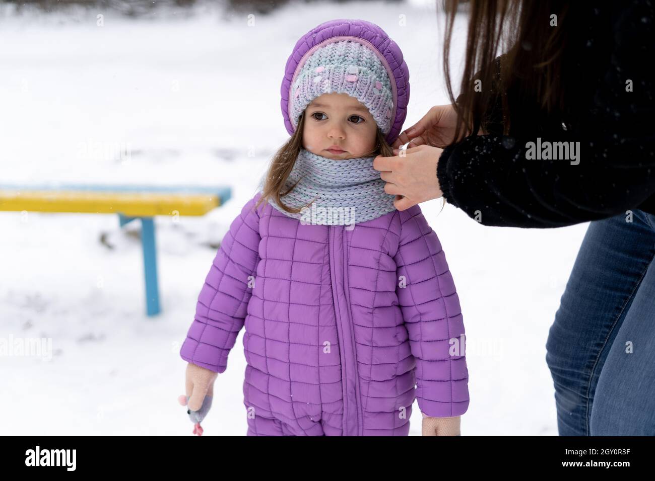 en hiver, une petite fille d'âge préscolaire se tient sur la neige.Maman redresse le foulard de bébé. Banque D'Images