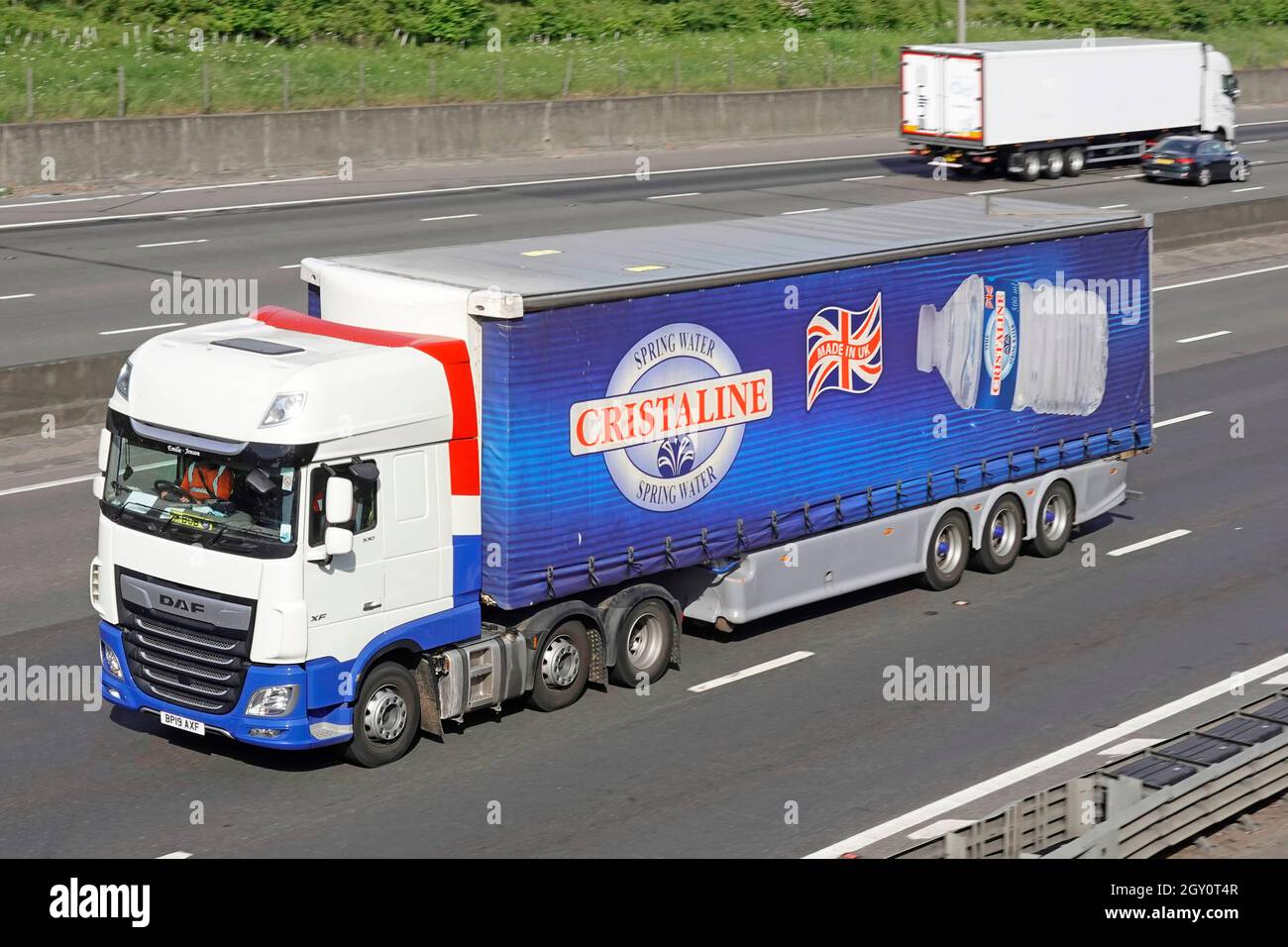 Vue avant et latérale camion Daf blanc et Cristaline bleu bouteille eau de printemps une publicité commerciale française sur bande-annonce à rideaux souples sur l'autoroute britannique Banque D'Images