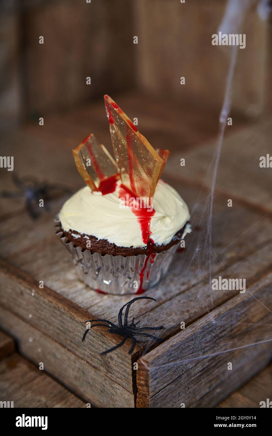 Halloween traitez le cupcake au chocolat avec une glaçage blanc et des éclats de verre qui suinent la sauce au sang rouge Banque D'Images