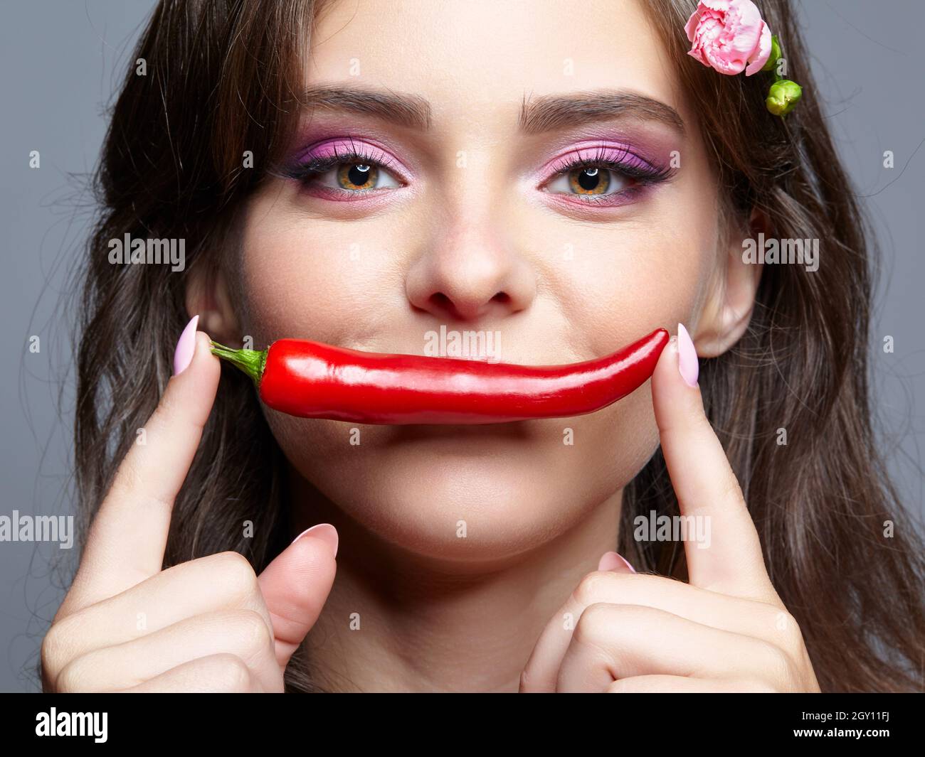 Portrait de la belle brune femelle avec piment cayenne rouge chaud épicé près de la bouche Banque D'Images