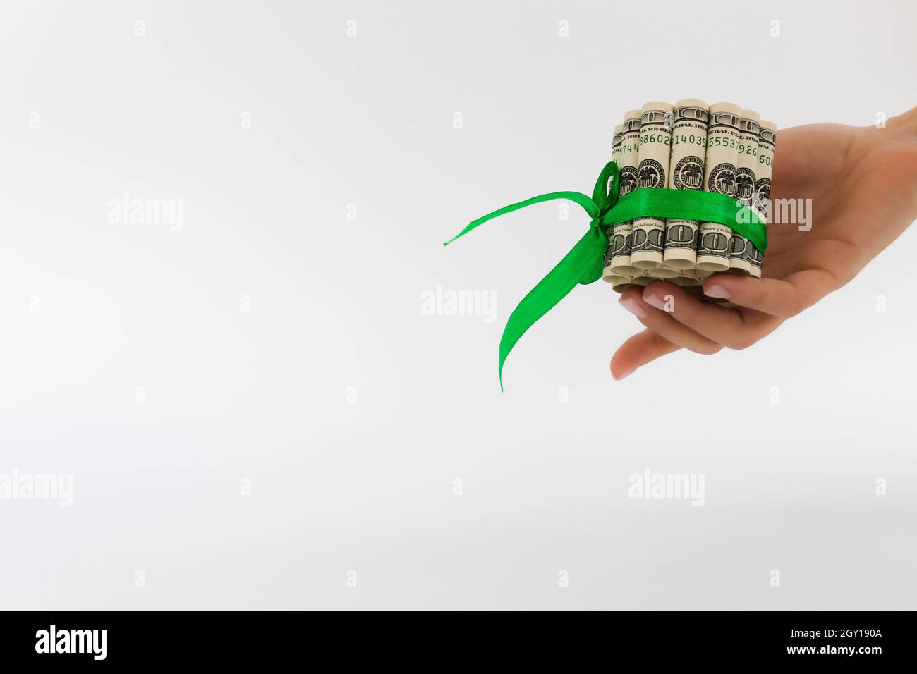 Main féminine tenant des billets roulés de 100 dollars liés avec ruban cadeau vert. Banque D'Images