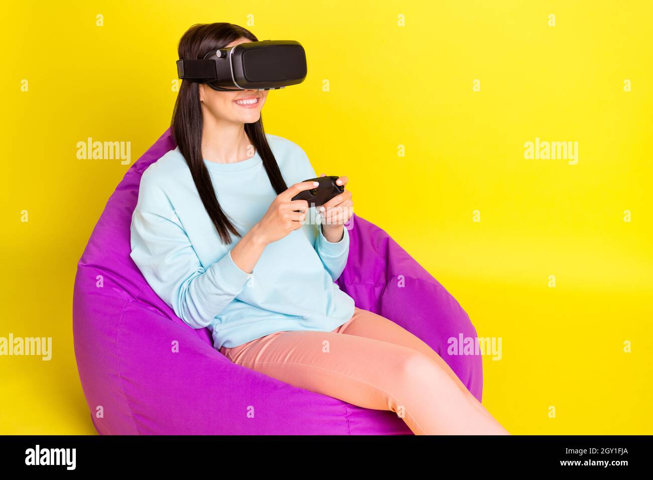 Photo de cool Brown hairdo jeune femme assis sur le sac jouer playstation show okey signe porter pantalon à capuche isolé sur fond jaune Banque D'Images