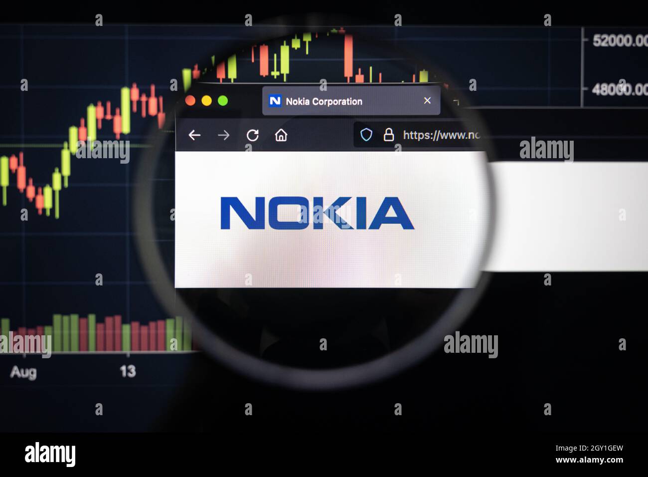 Logo de la société Nokia sur un site web avec des développements flous de marché boursier en arrière-plan, vu sur un écran d'ordinateur à travers une loupe Banque D'Images