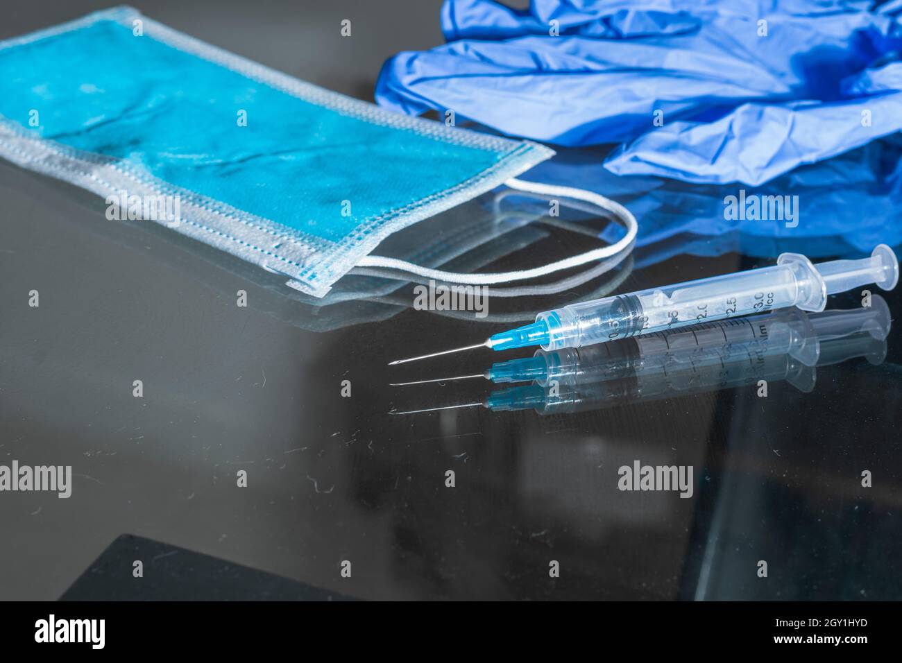 seringue, masque de protection hygiénique et gants bleus, sur la table en verre, instruments de vaccination (covid-19, grippe) ton contraste foncé, pandem Banque D'Images