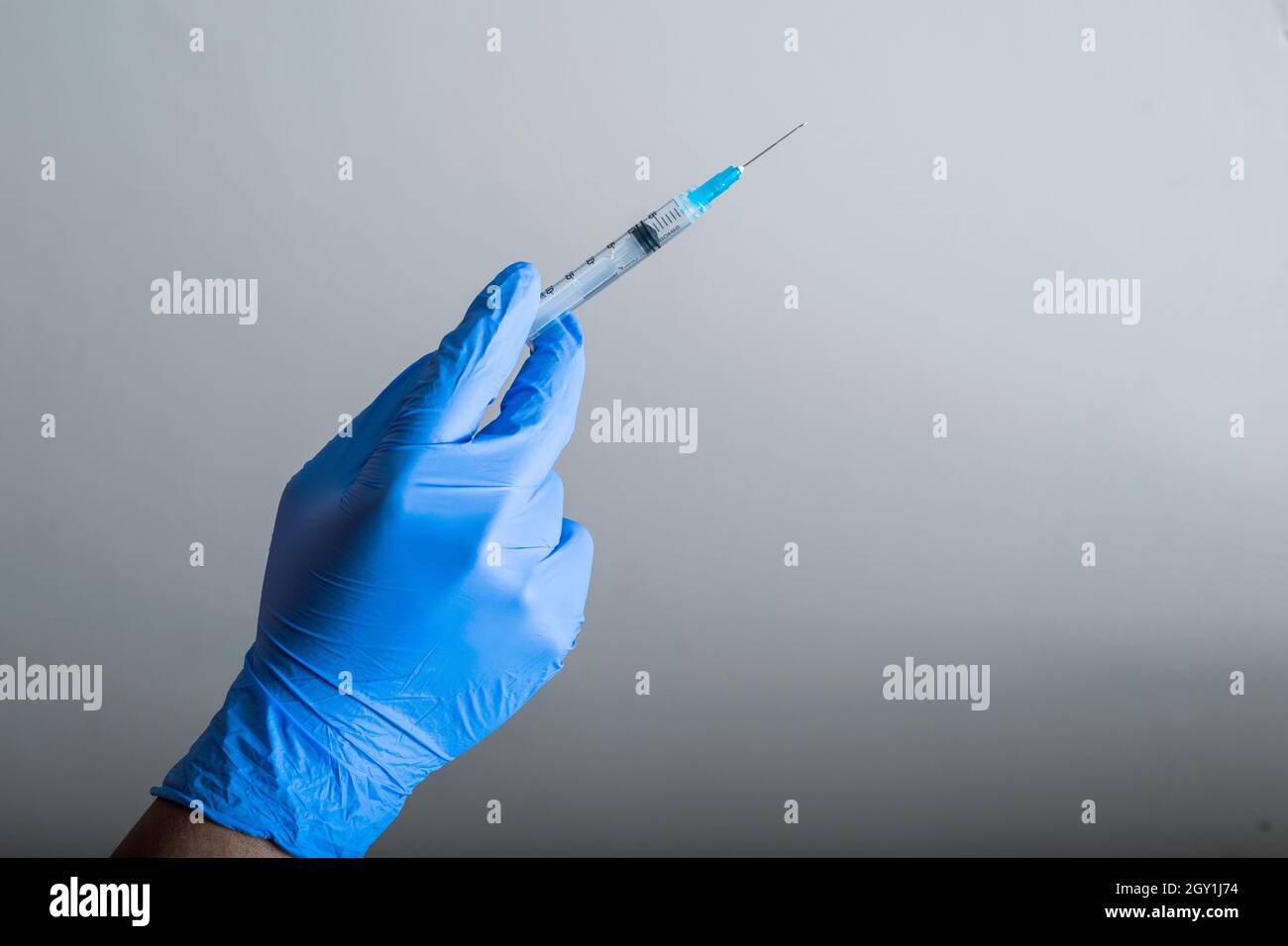 main du médecin avec des gants en caoutchouc bleu, tenant une seringue prête pour la vaccination, fond gris dégradé. outils de vaccination (covid-19, grippe) pand Banque D'Images