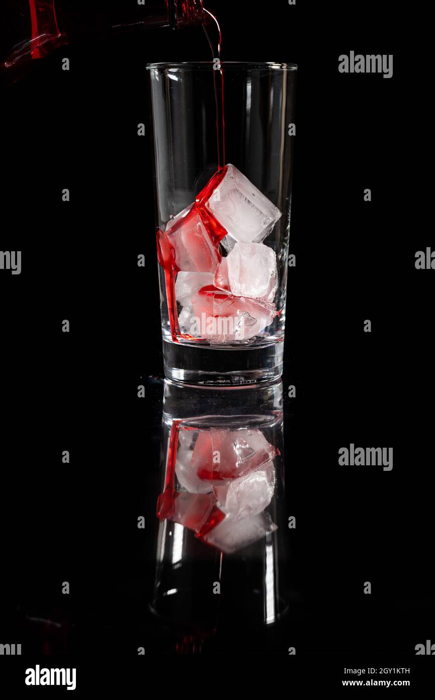 Verser la solution rouge non alcoolique sur le dessus de la glace dans le verre sur fond noir complet.Pour l'alcool, concept de cave de vinification. Banque D'Images