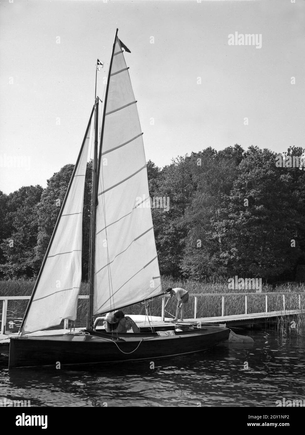 Ein einem Segelboot beim Ablegen une Holzsteg Am Ufer eines voit, Deutschland 1930er Jahre. Un bateau à voile retiré le peigne d'une promenade à la rive d'un lac, l'Allemagne des années 1930. Banque D'Images