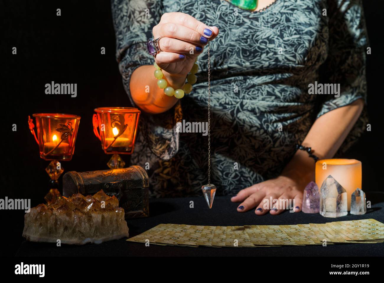 Détail des mains d'une femme passant un pendule sur un jeu de cartes de tarot.Concept d'une session de divination avec des cartes de tarot. Banque D'Images