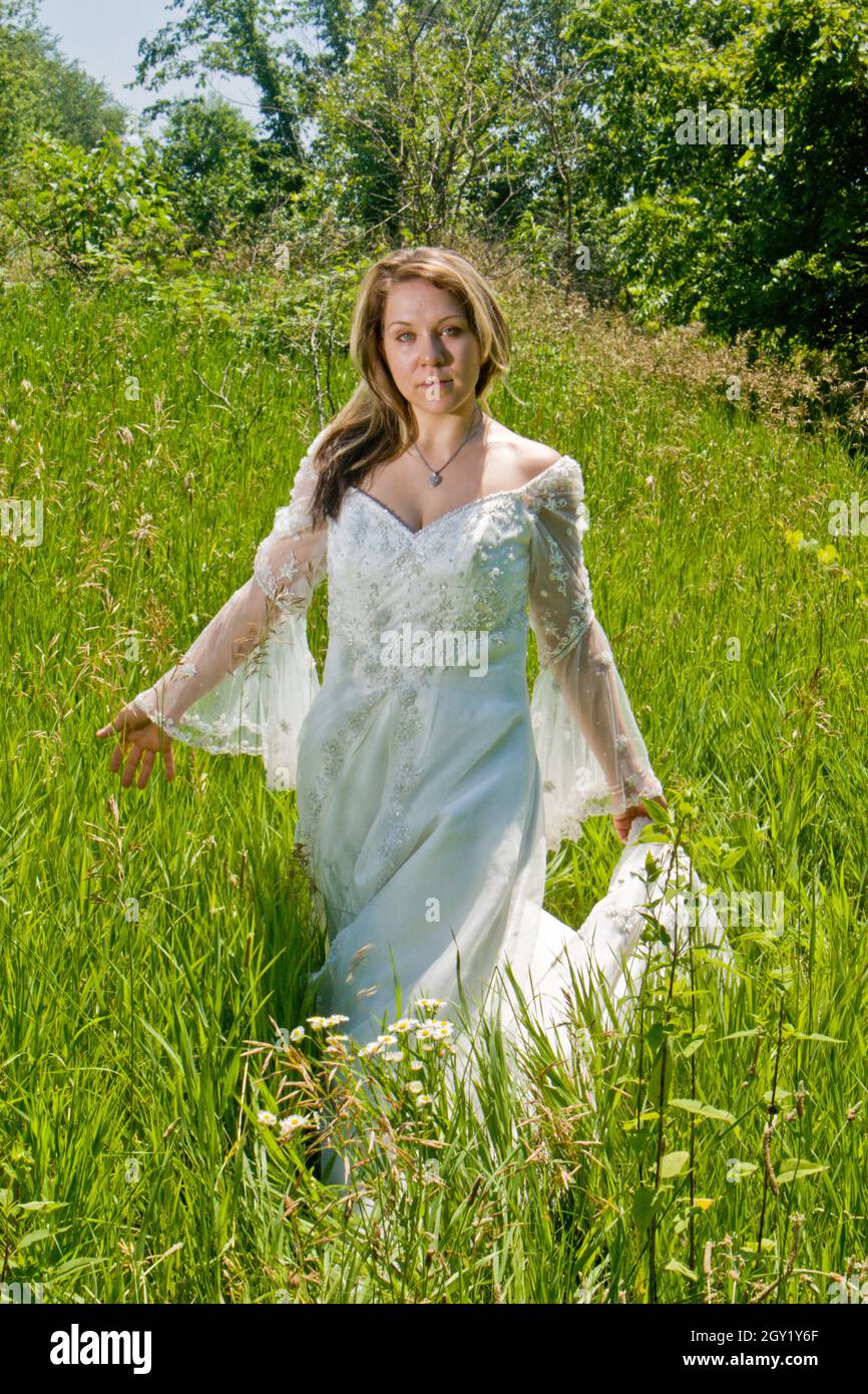 Belle femme avec de longs cheveux bruns dans une robe blanche fluide dans un pré parmi de grandes herbes Banque D'Images