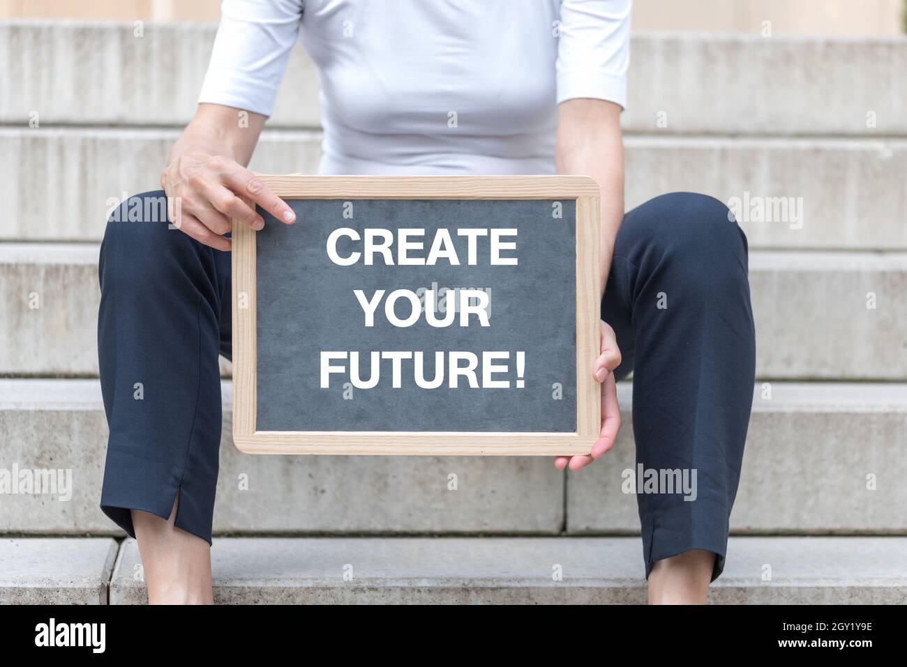 Femme d'âge moyen assise dans les escaliers et tenant un tableau noir avec le texte « Create Your future! » Banque D'Images