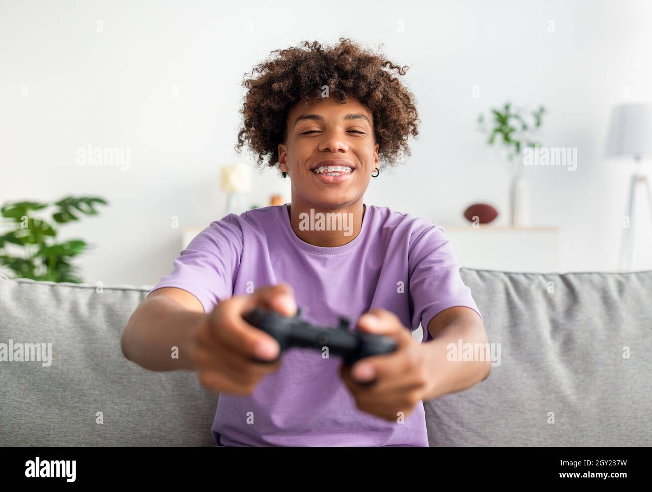 Divertissements domestiques.Joyeux garçon noir adolescent avec joystick jouant en ligne jeux d'ordinateur sur le canapé à la maison Banque D'Images