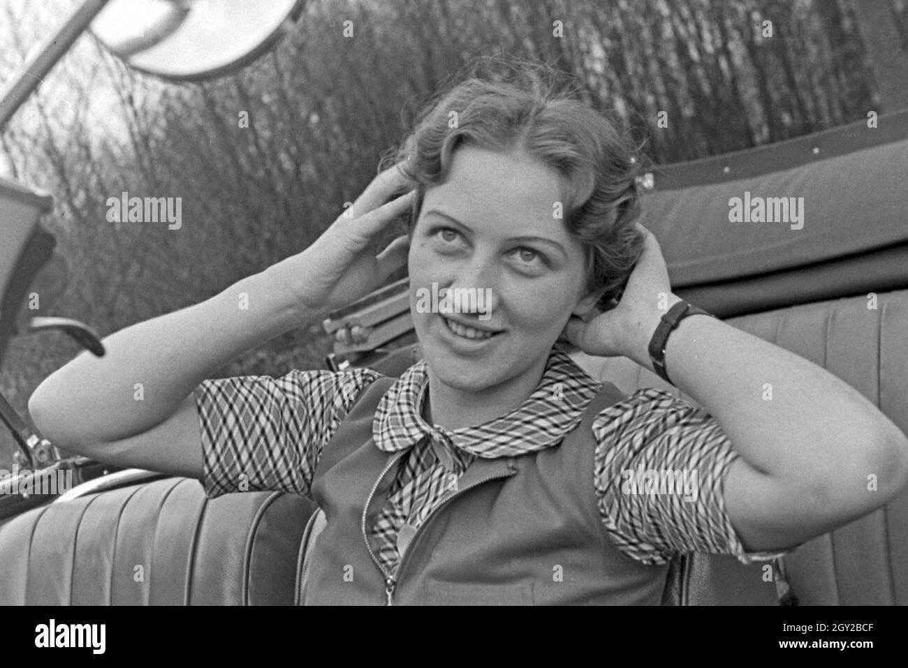 Eine junge Frau schminkt sich im Seitenspiegel votre Cabrios, Deutschland 1930er Jahre. Une jeune femme contrôler son faire dans le miroir de l'aile de son cabriolet, Allemagne 1930. Banque D'Images