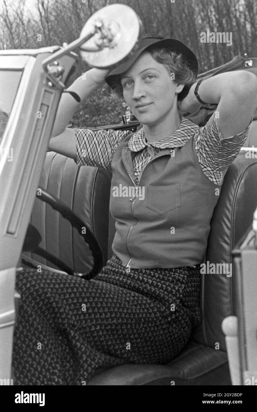 Eine junge Frau schminkt sich im Seitenspiegel votre Cabrios, Deutschland 1930er Jahre. Une jeune femme contrôler son faire dans le miroir de l'aile de son cabriolet, Allemagne 1930. Banque D'Images