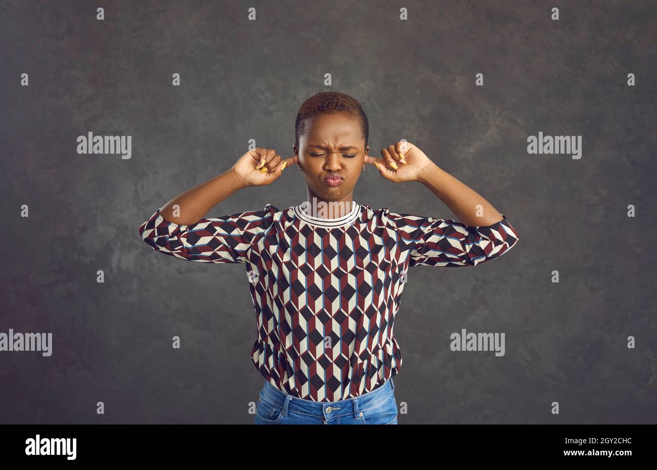 Une jeune femme afro-américaine capricieuse couvre ses oreilles avec ses doigts pour ne rien entendre. Banque D'Images