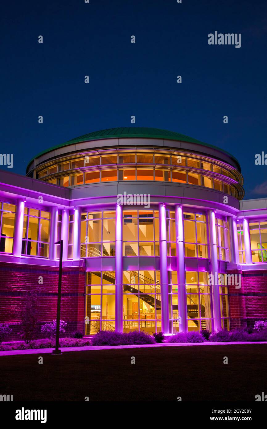Prenez la photo de la porte d'entrée du bâtiment moderne avec de nombreuses fenêtres au crépuscule éclairées en violet Banque D'Images