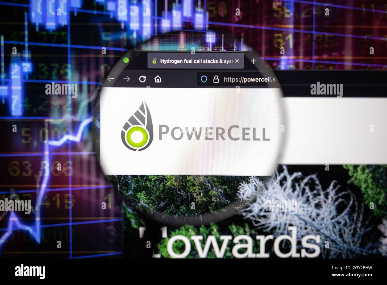 Logo de la société PowerCELL sur un site web avec des développements flous du marché boursier en arrière-plan, vu sur un écran d'ordinateur à travers une loupe Banque D'Images