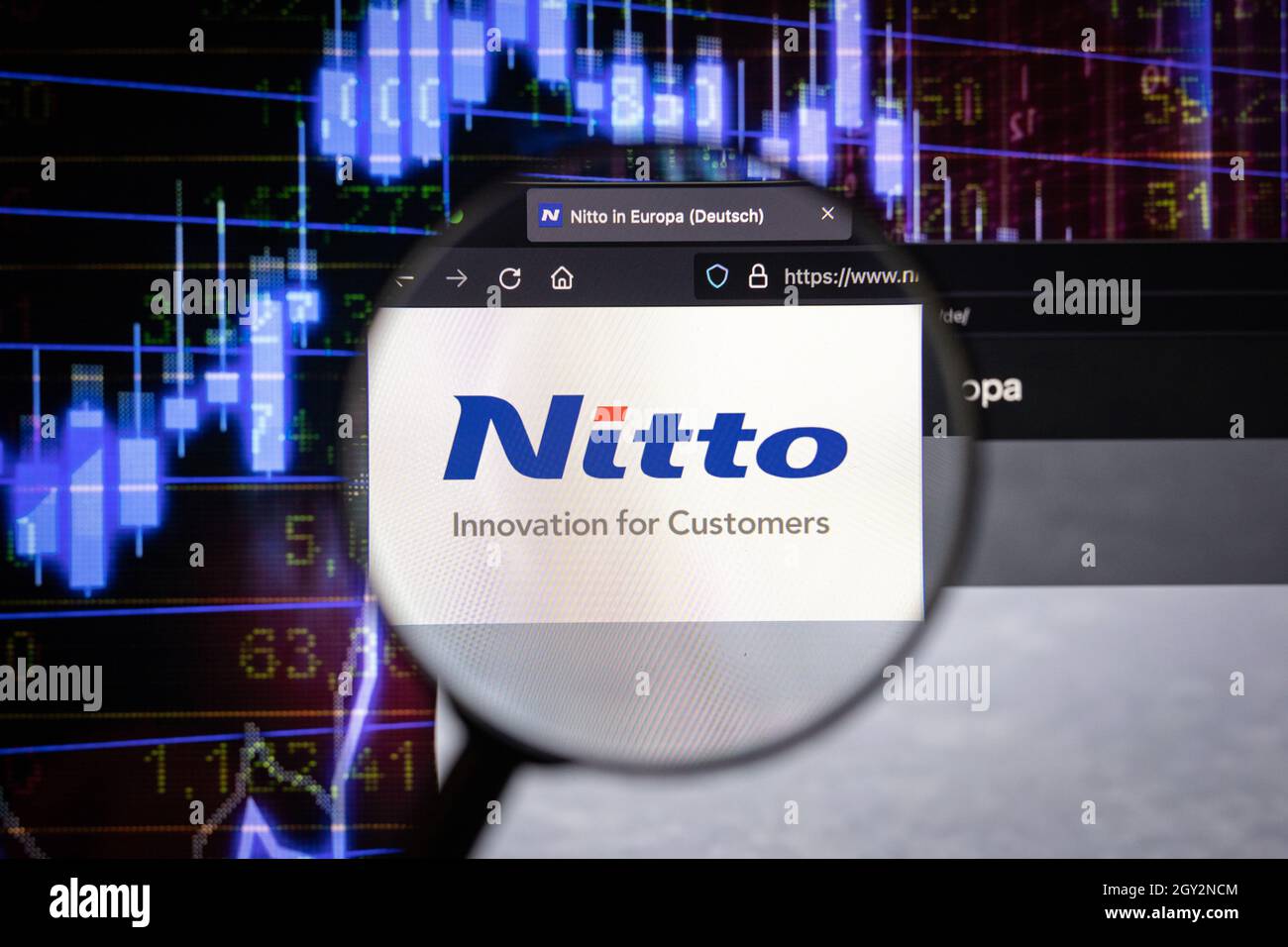 Le logo de la société Nitto sur un site web avec des développements flous du marché boursier en arrière-plan, vu sur un écran d'ordinateur à travers une loupe Banque D'Images