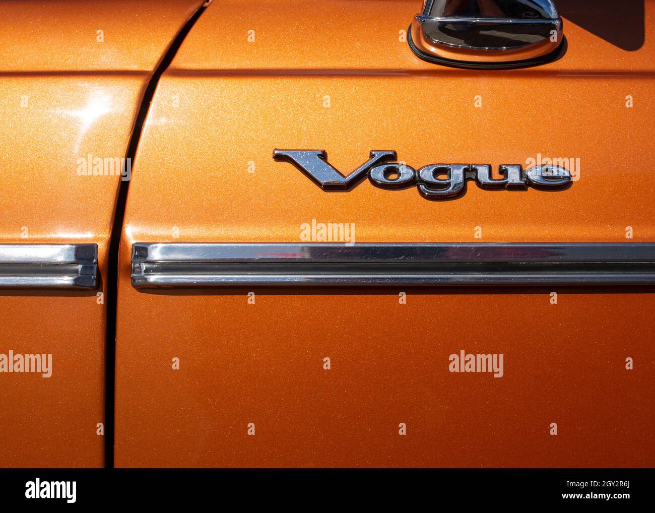 Image de l'écusson chromé sur la porte latérale d'une voiture Sunbeam Vogue des années 1970, le mot Vogue au-dessus d'une bande de porte chromée sur une peinture orange métallique Banque D'Images