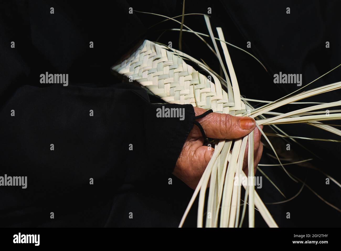 Mains de femme arabe âgée artisan en robe noire traditionnelle gros plan panier de tissage à partir de feuilles de palmier organiques séchées. Banque D'Images