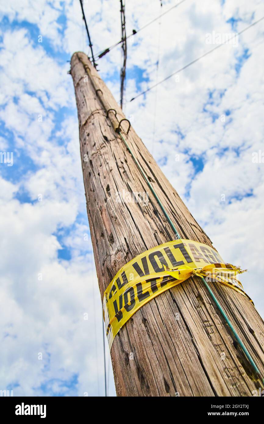 Vue sur le poteau téléphonique en bois avec un ruban d'avertissement de tension jaune Banque D'Images