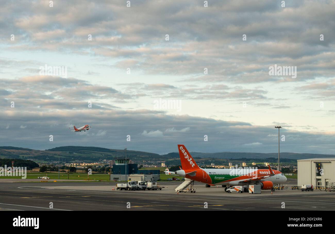 Un Airbus A320-200 easyJet avec une publicité Europcar garée sur le tablier à l'aéroport de Glasgow, en Écosse, tandis qu'un autre avion Easyjet départ. Banque D'Images