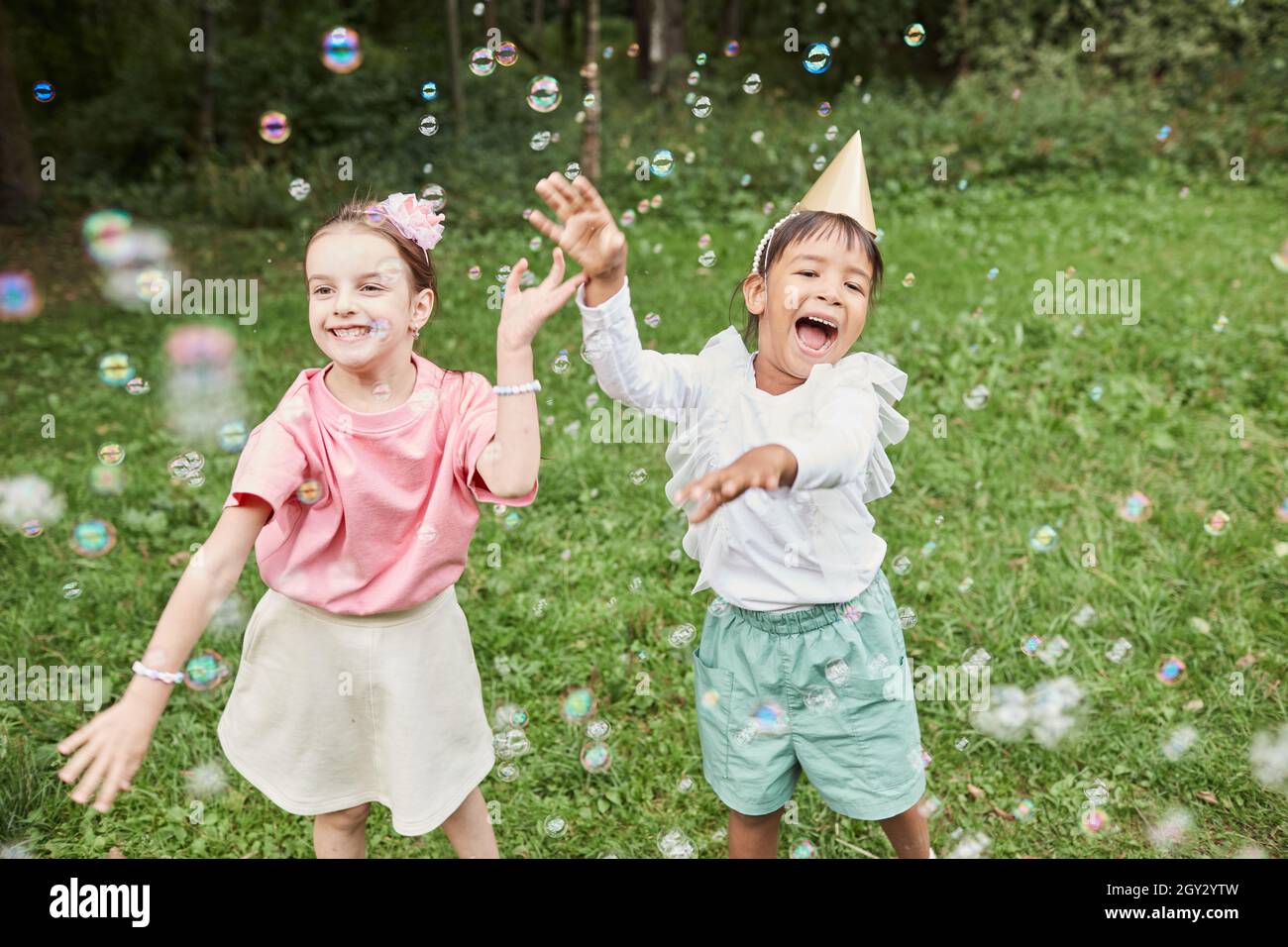 Portrait de deux jolies filles jouant avec des bulles tout en appréciant la fête d'anniversaire dehors en été Banque D'Images
