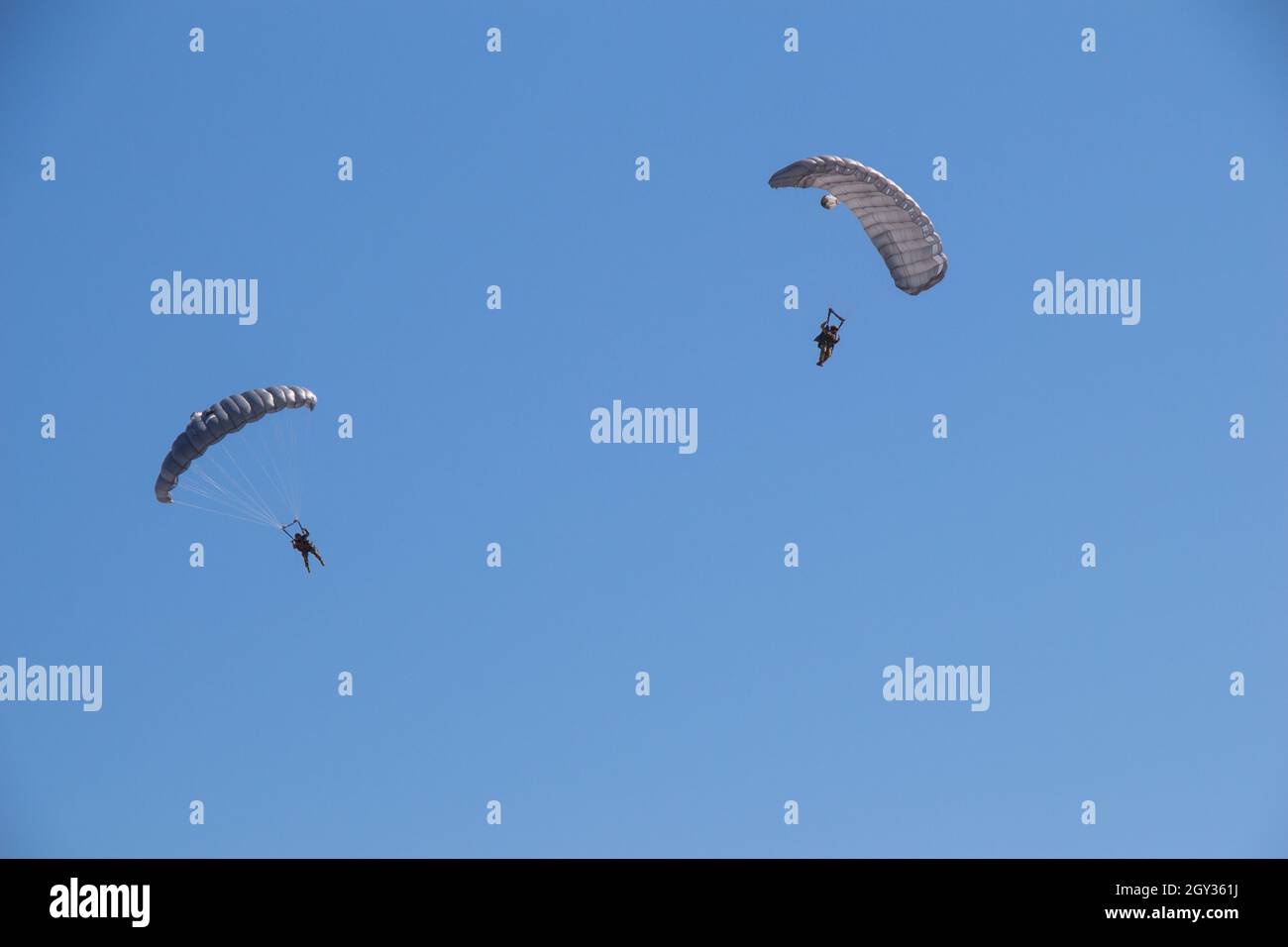 Deux personnes aventureuses volant dans le ciel bleu vif avec des parachutes Banque D'Images