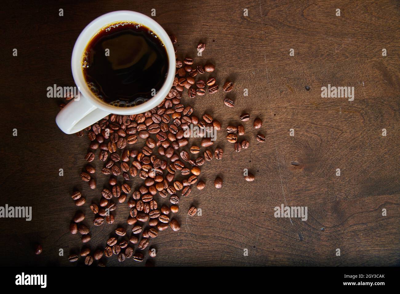 Tasse de café et grains de café éparpillés sur une surface en bois sombre Banque D'Images