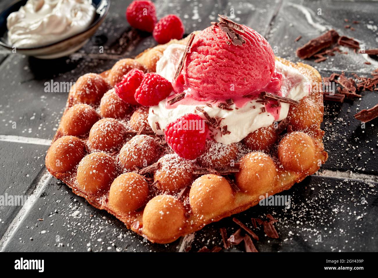 Délicieuse gaufre à bulles recouverte de crème glacée à la framboise et de baies rouges mûres fraîches garnies de flocons de chocolat sur un lit de crème fouettée Banque D'Images