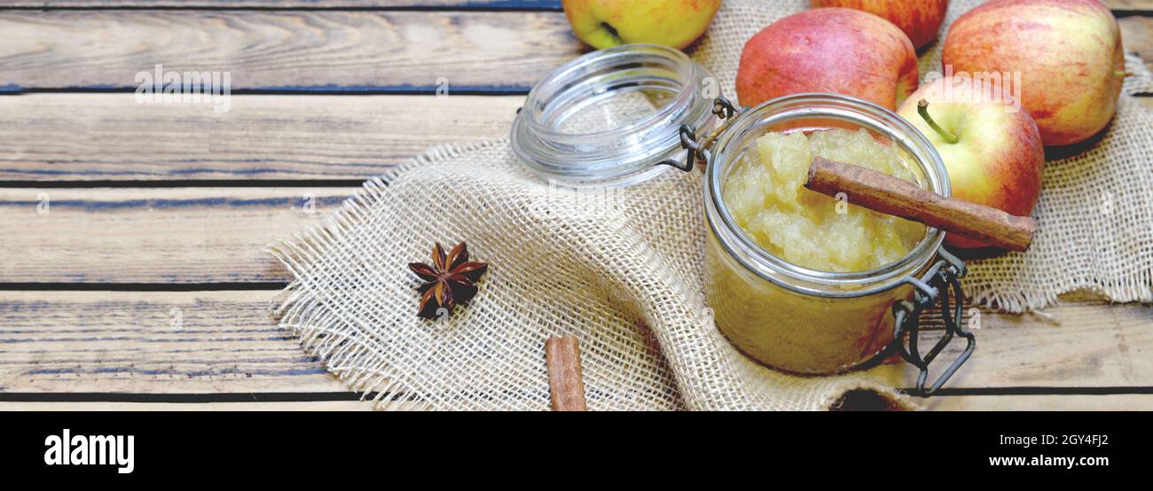 sauce aux pommes maison dans un pot en verre avec des pommes rouges et un bâton de cannelle sur une table en bois Banque D'Images