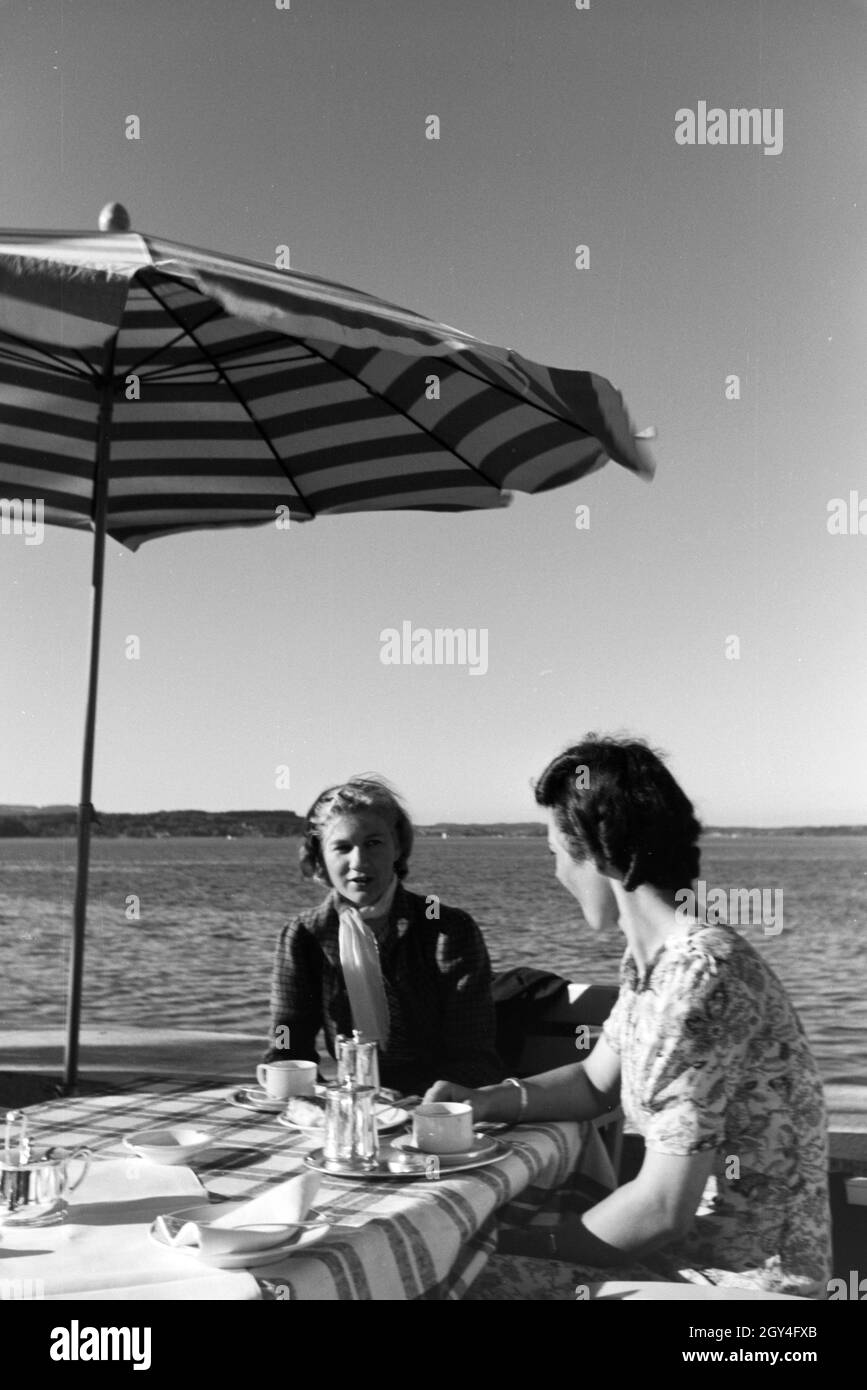 Junge Frauen trinken Kaffee auf der Sonnenterrasse eines cafés am Chiemsee, Deutschland 1930.Les jeunes femmes savourent une tasse de café sur la terrasse ensoleillée d'un café du Chiemsee, Allemagne des années 1930. Banque D'Images