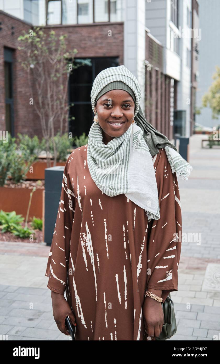 Portrait d'une femme musulmane africaine en hijab souriant à la caméra tout en se tenant dans la ville Banque D'Images