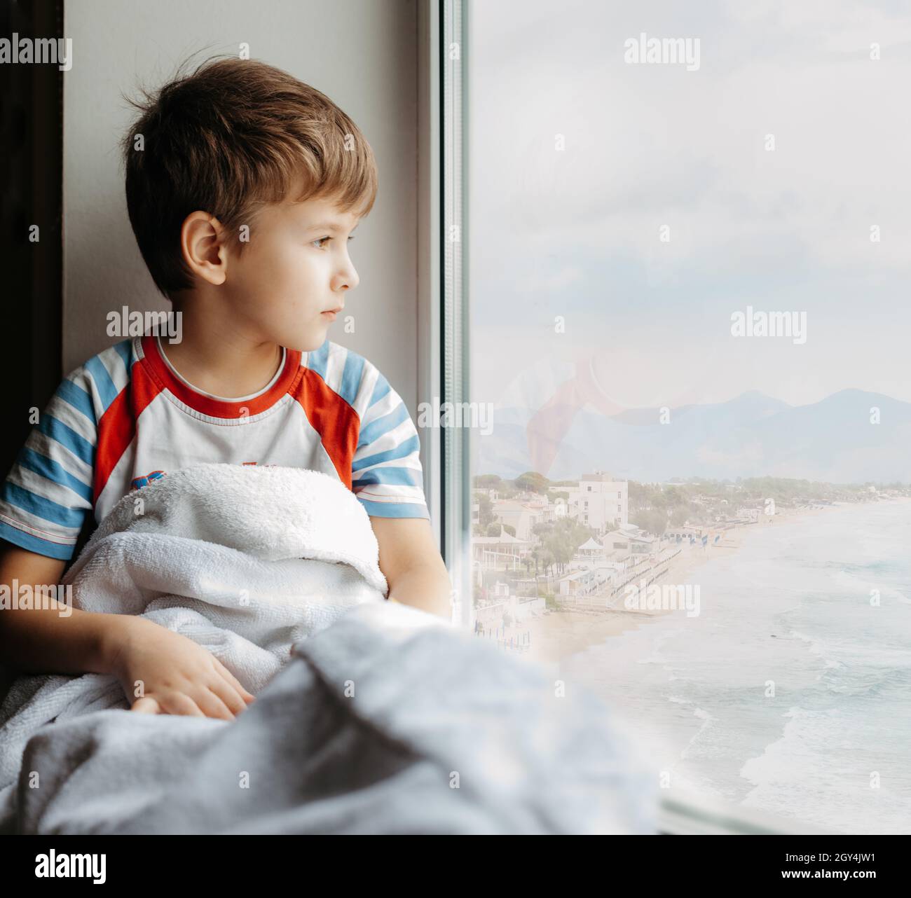 Triste petit garçon assis à la maison en quarantaine.Un enfant malade s'assoit près de la fenêtre et regarde la mer Banque D'Images