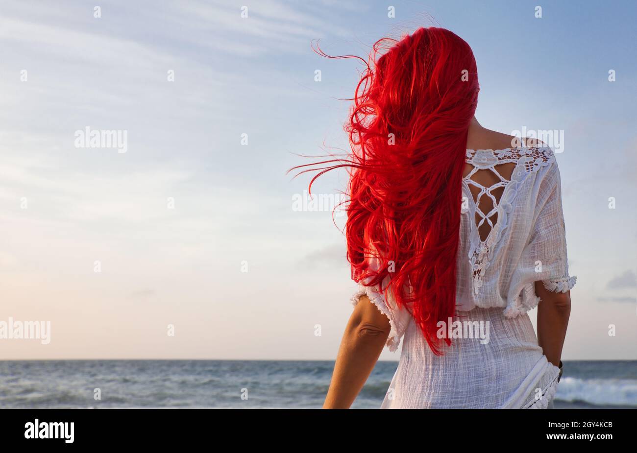 Vue arrière d'une belle femme aux cheveux rouges appréciant le coucher de soleil sur la plage Banque D'Images