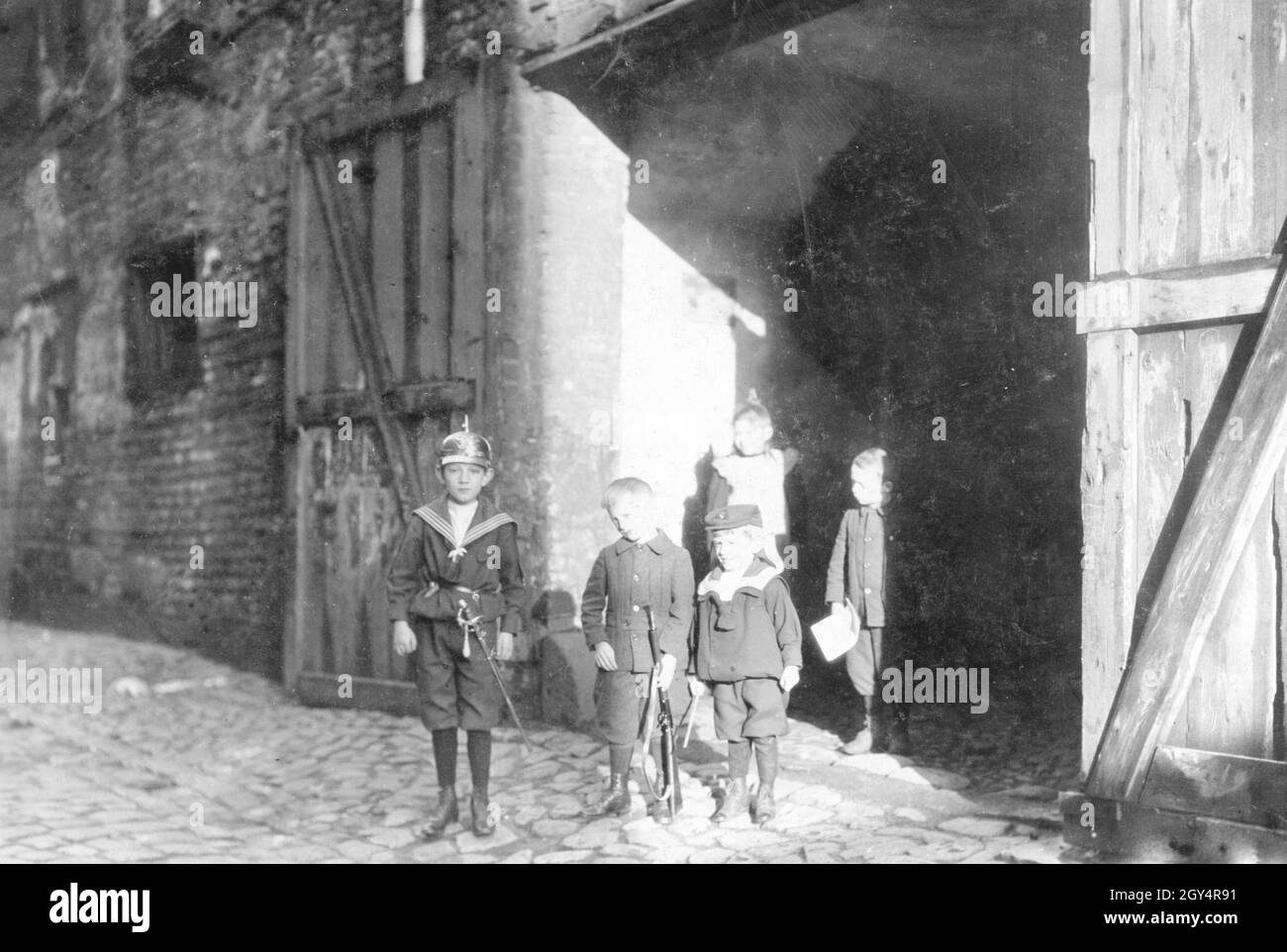 Cinq enfants, vraisemblablement frères et sœurs, se tiennent dans une entrée de cour dans la ruelle Am Krögel à Berlin-Mitte en 1907, portant des uniformes et des armes de jouet.[traduction automatique] Banque D'Images