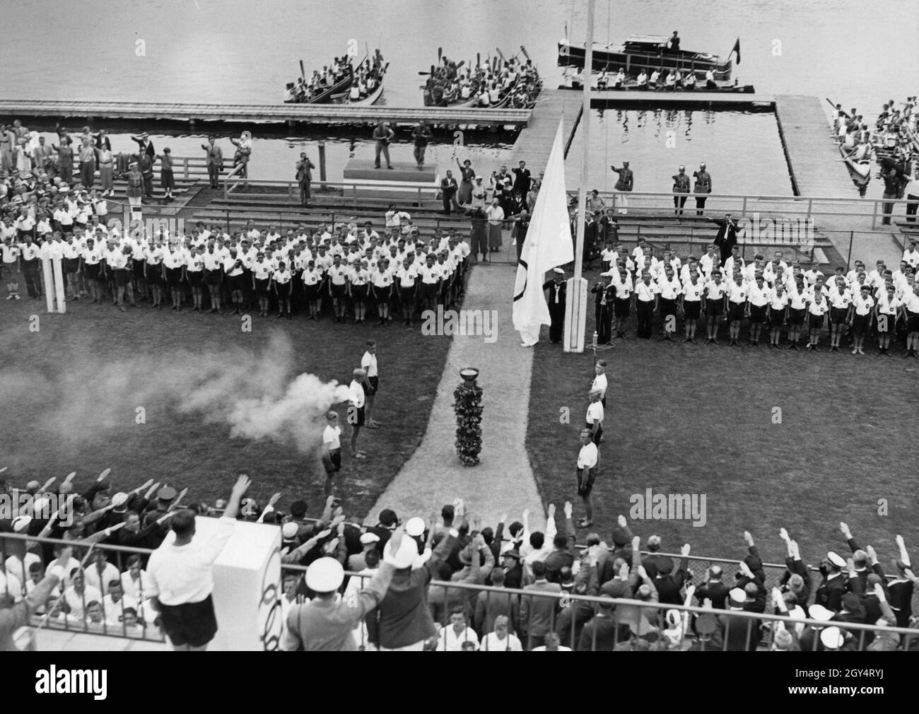 Un grand drapeau olympique a été hissé à l'ouverture des Jeux Olympiques d'aviron, qui ont eu lieu entre le 11 et le 14 août au cours de régate de Grünau près de Berlin.Des spectateurs dans les tribunes ainsi que des journalistes et des policiers ont montré le salut d'Hitler.Les compétitions de canoë ont eu lieu sur le même cours déjà à partir d'août 7, donc la photo aurait pu être prise le 7 août.[traduction automatique] Banque D'Images