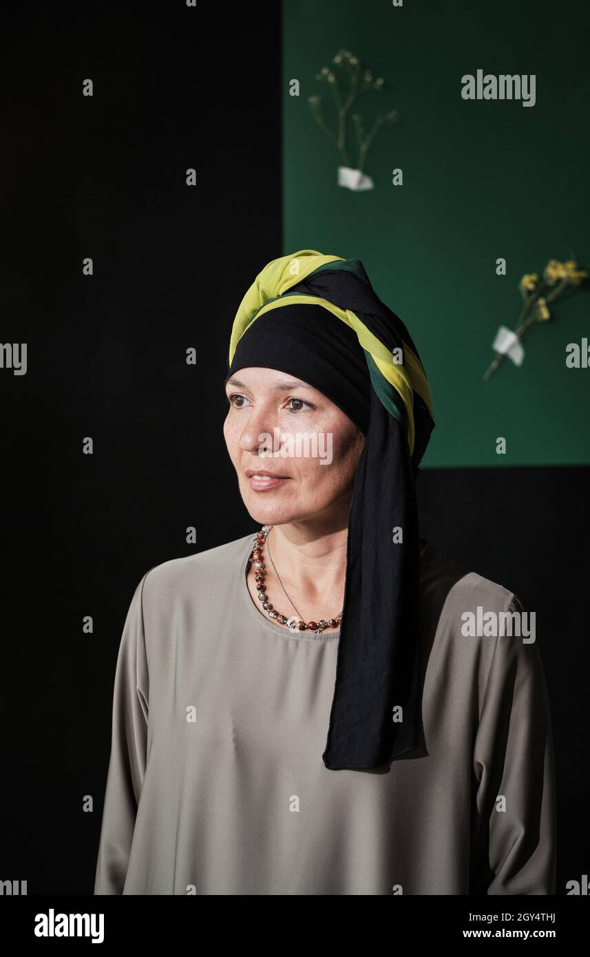 Portrait d'une femme mûre élégante vêtue de vêtements musulmans en regardant loin contre le mur moderne Banque D'Images