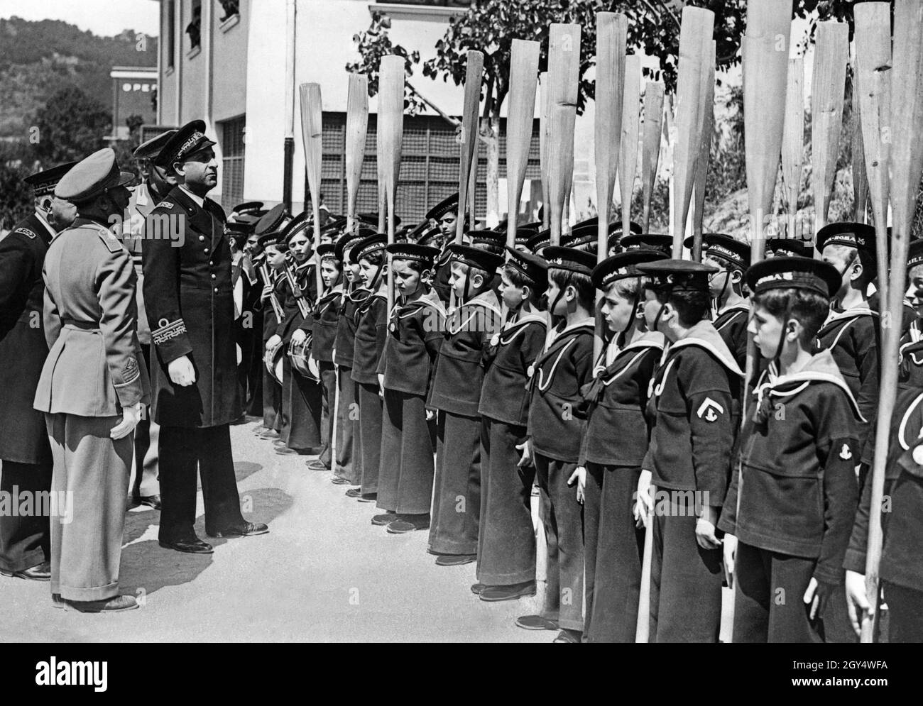 Un amiral arrière de la Marine italienne (4ème de gauche), avec d'autres officiers, examine de façon critique la formation des garçons Marinaretti, qui sont censés tenir leurs oars à l'attention.La photo a été prise en 1935 dans la cour de la Maison Balilla du Marinaretti à Rome, une école navale de l'Opéra Nazionale Balilla.[traduction automatique] Banque D'Images