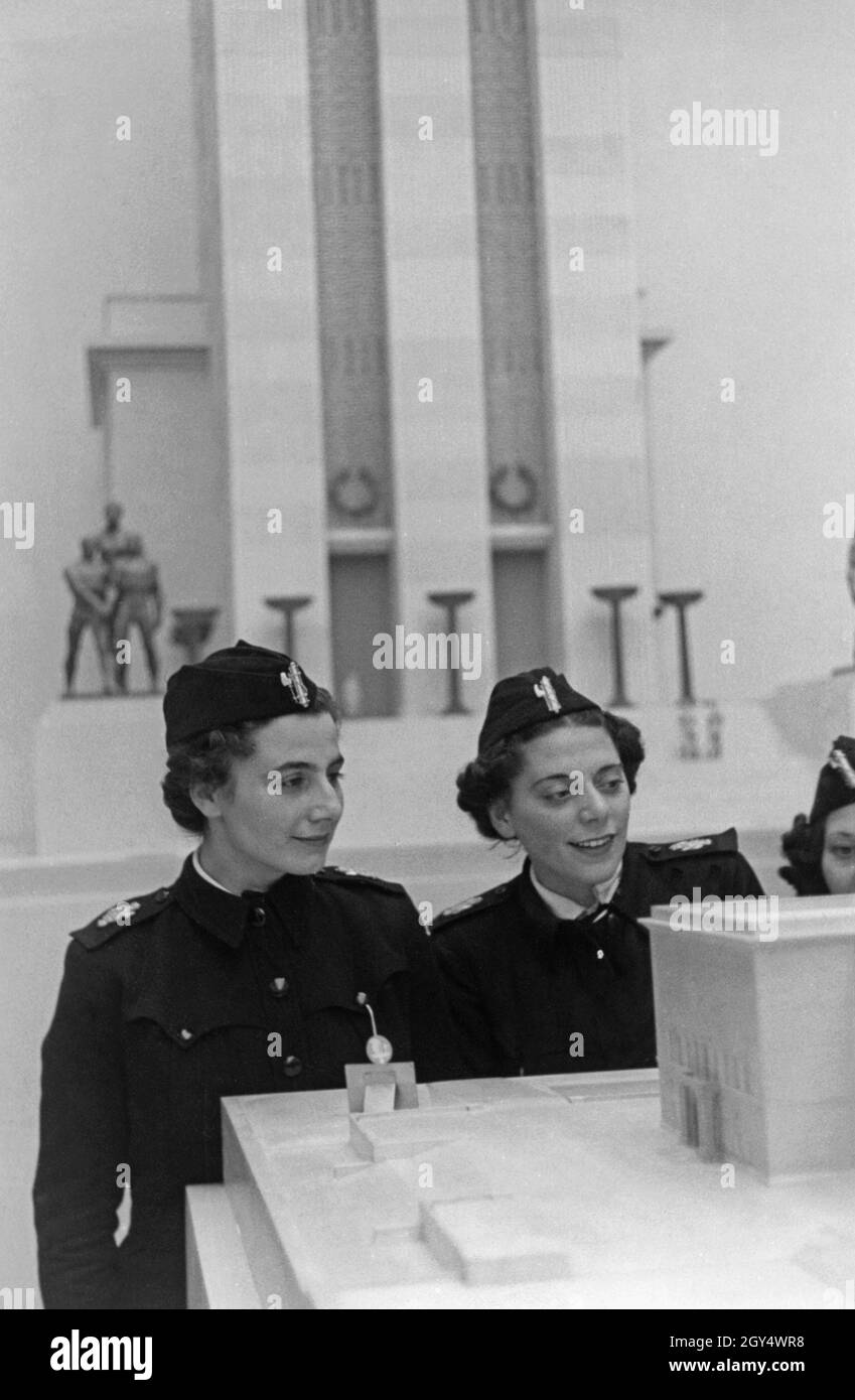 L'image montre trois jeunes femmes d'Italie qui appartiennent à l'Opéra fasciste Nazionale Dopolavoro (OND).Ils sont dans l'antichambre de la Haus der Deutschen Kunst (aujourd'hui Haus der Kunst) à Munich, où ils regardent des modèles architecturaux montrant les plans allemands nazis pour des bâtiments plus monumentaux.Les femmes italiennes ont pu partir en vacances à Munich par l'intermédiaire de l'OND.L'OND était l'organisation de loisirs et de loisirs des fascistes italiens et l'organisation fasciste de masse avec le plus grand nombre de membres.Photographie non datée, probablement prise à la fin des années 1930.[traduction automatique] Banque D'Images