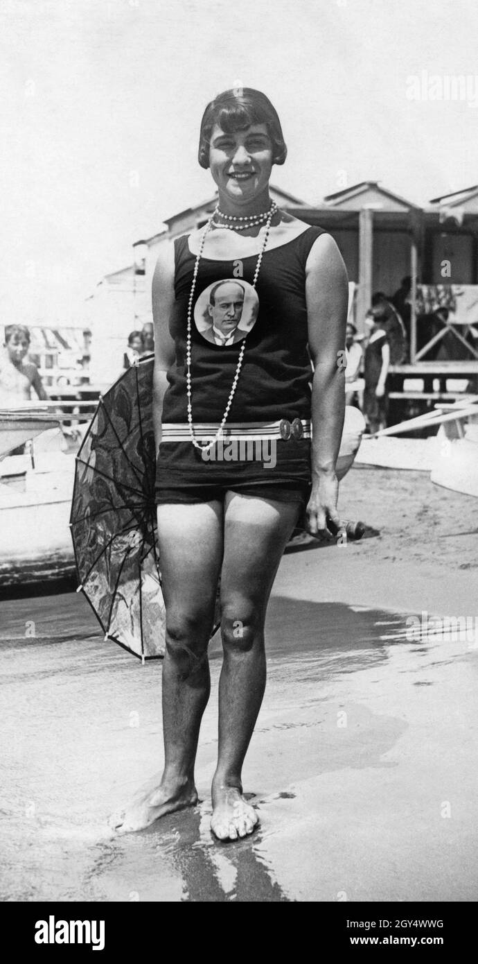 La photo montre une femme sur la plage d'Anzio au sud de Rome.Elle porte un  maillot de bain avec une empreinte de Benito Mussolini.La photographie a  été prise le 7 juillet 1929.[traduction