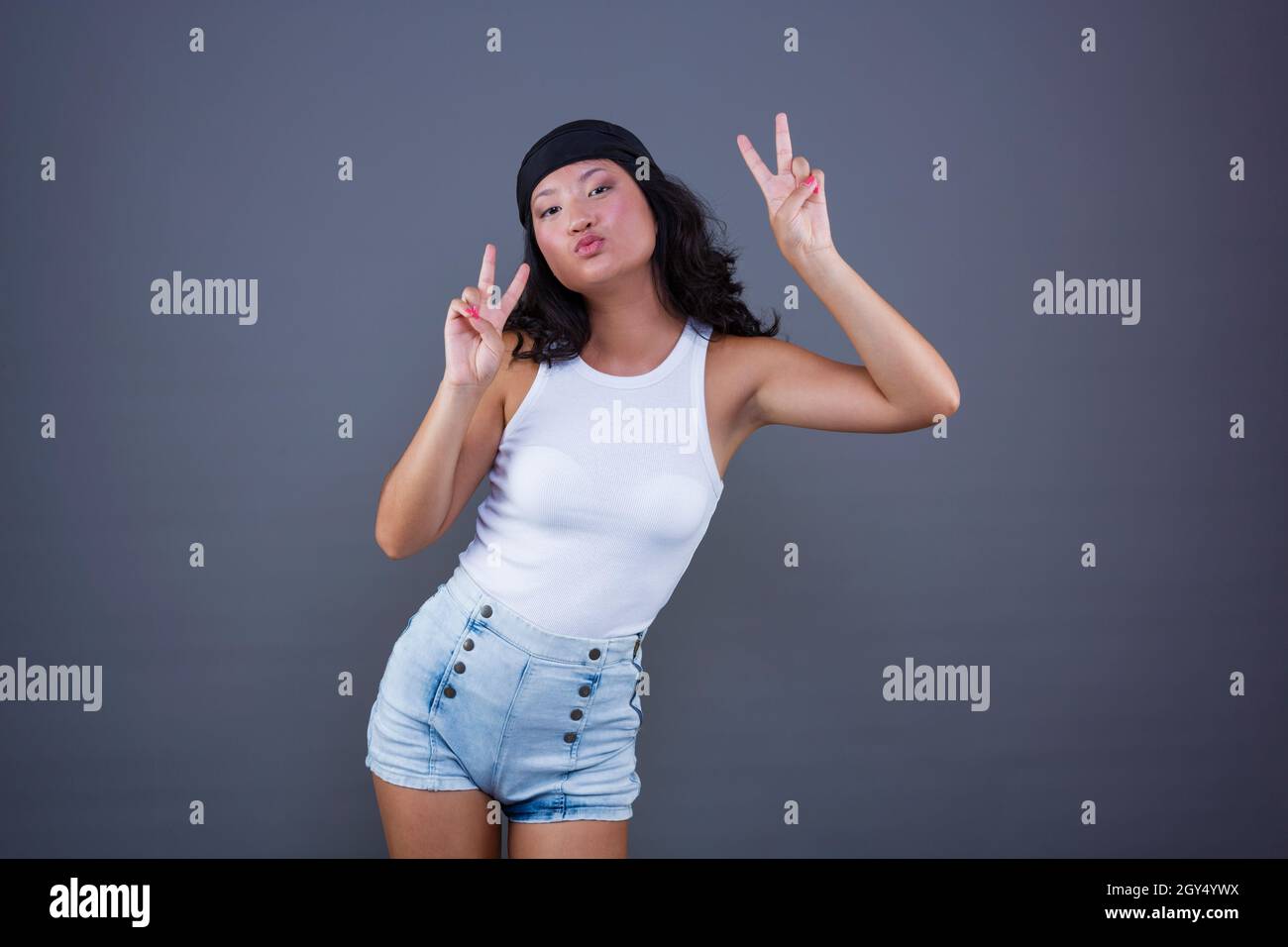 jeune fille chinoise avec bandana et short, faisant le signe de la paix ou de la victoire, dans une posture et une expression drôles. Banque D'Images