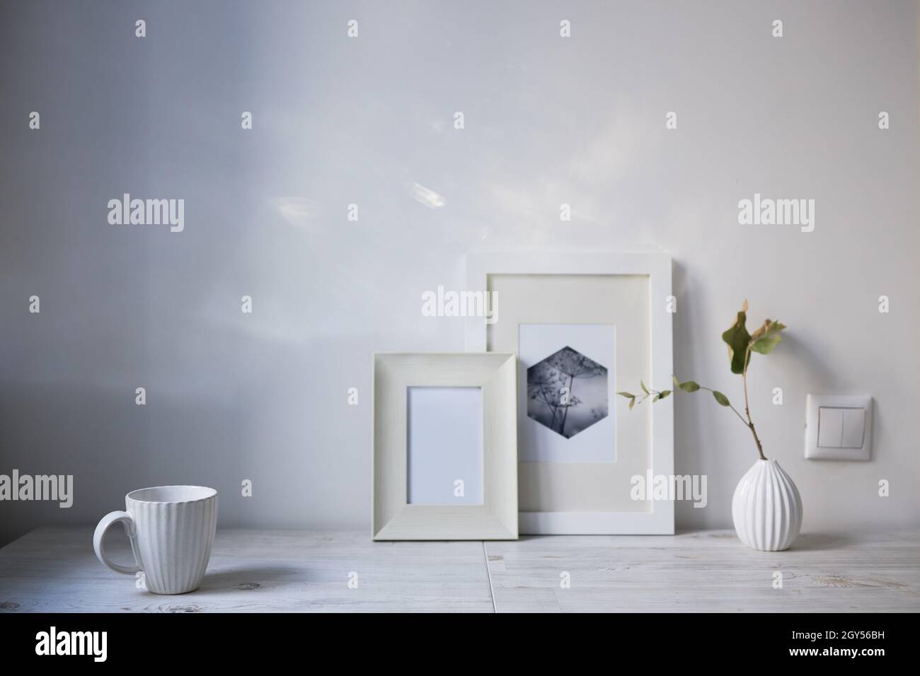 Style scandinave. Design intérieur. Une tasse blanche, un petit vase avec une branche d'eucalyptus séché, deux cadres photo sont sur la table. Copier l'espace pour tex Banque D'Images