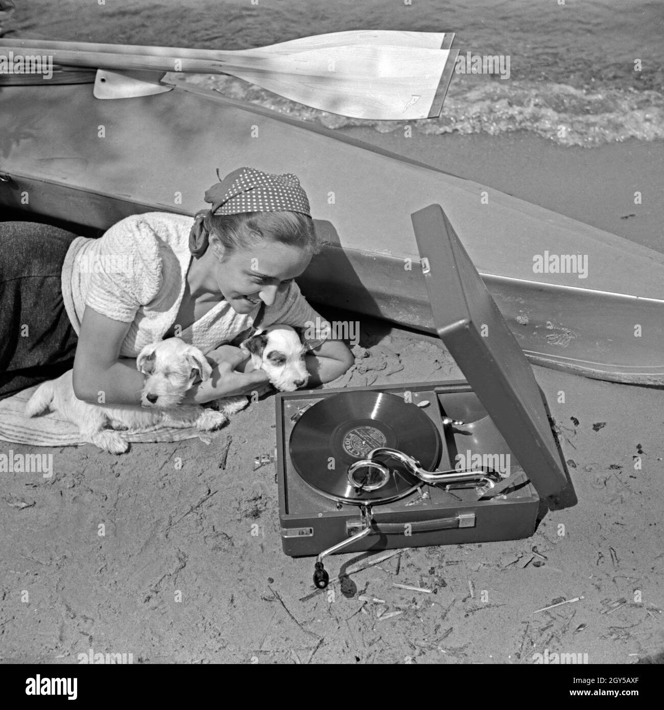 Werbefoto für das Klepper Faltboot : eine junge Frau mit zwei liegt und einem a diet Grammophon am Strand von voit und hört eine Electrola Schellackplatte, 1930er Jahre Deutschland. Un foldboat publicité für Klepper : une jeune femme avec deux chiots se trouvant sur la plage de l'écoute d'un gramophone, Allemagne 1930. Banque D'Images